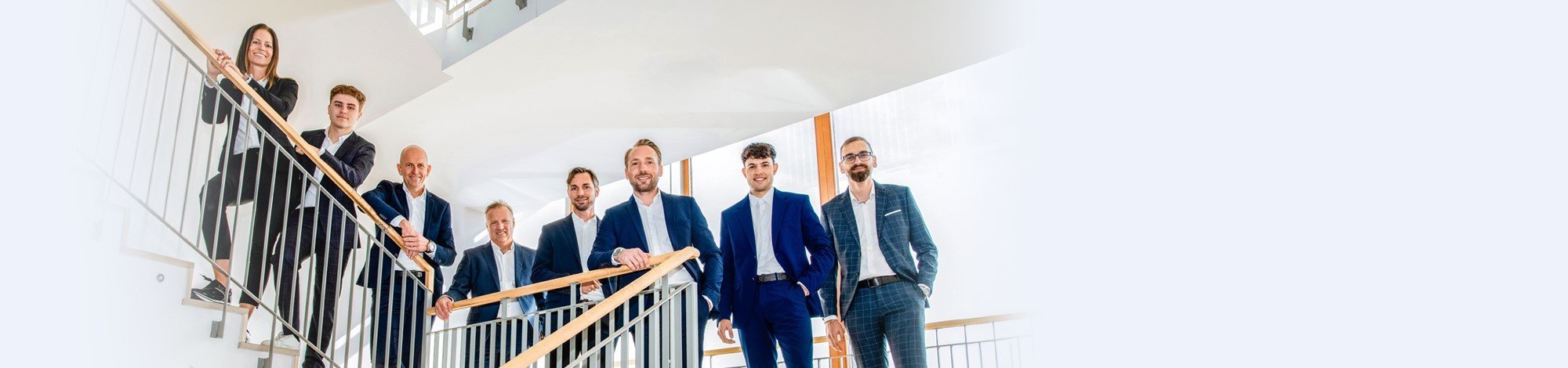 Das Team der Generalagentur Wals-Siezenheim in blauen Anzügen auf einem Treppenaufgang.